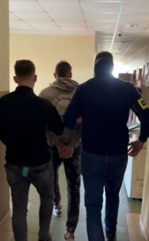 Zatrzymany siedzi na krzesle obok stoją policjanci