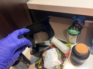 Zdjęcie przedstawia zatrzymanego oraz policjantów i ujawnione narkotyki.