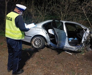 Zdjęcie przedstawia policjanta, pracującego przy wraku pojazdu.