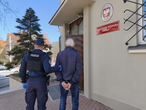 Zdjęcie przedstawia policjanta, doprowadzającego zatrzymanego do prokuratury.