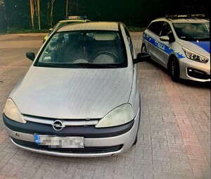 Zdjęcie przedstawia policjantów z zatrzymanym oraz ich pojazdy.