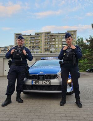 zdjęcie przedstawia dwoje policjantów na tle radiowozu